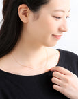 K18ゴールドのボールチェーンネックレスを着用したモデル。丸パーツと長丸パーツが繊細に輝き胸元を華やかに彩る、山梨県甲府市で製作したMITUREの18金ネックレス。