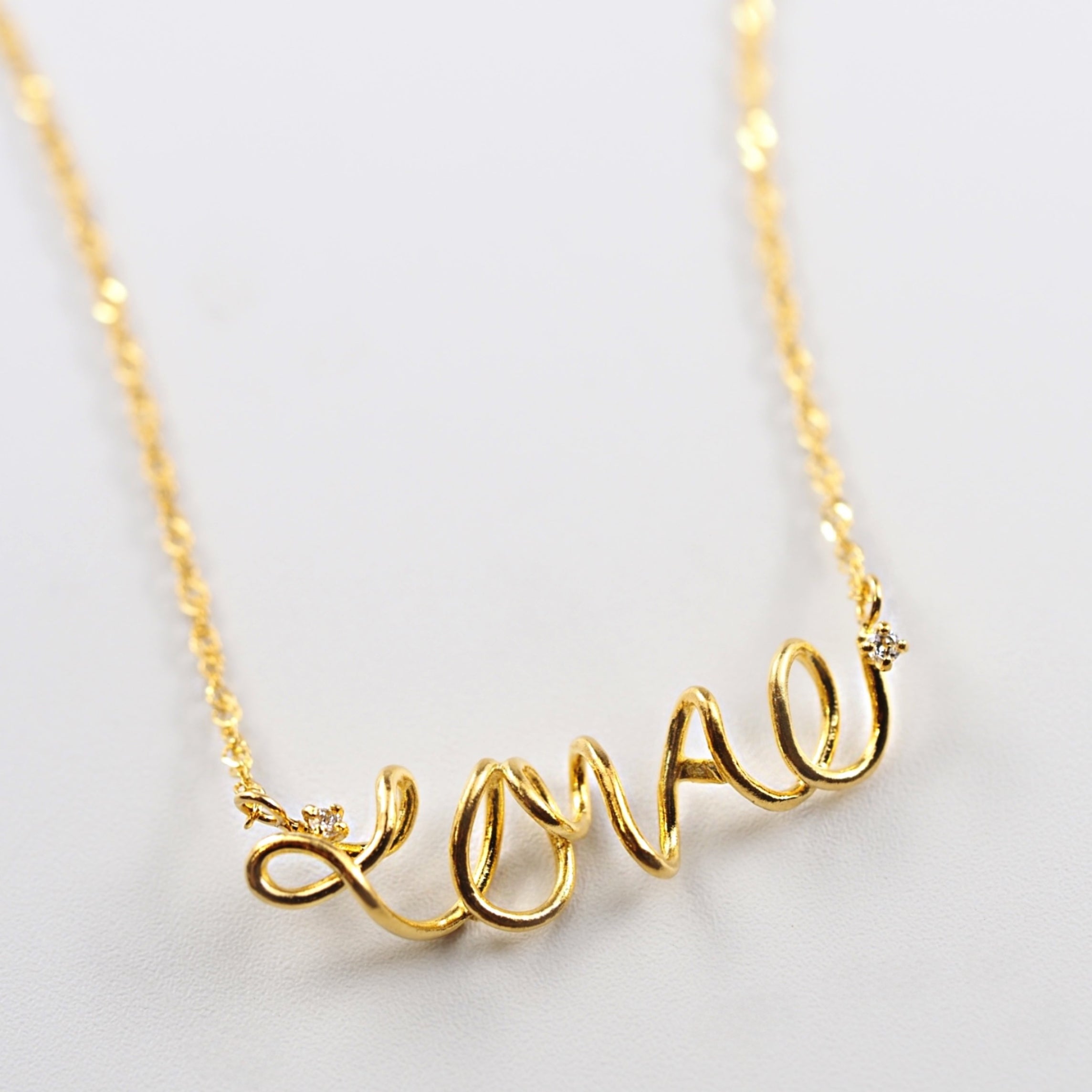 両サイドに添えたダイヤモンドが控えめに輝く、MITUREのLOVEネックレス。やわらかな黄金色と透明感が美しく調和。