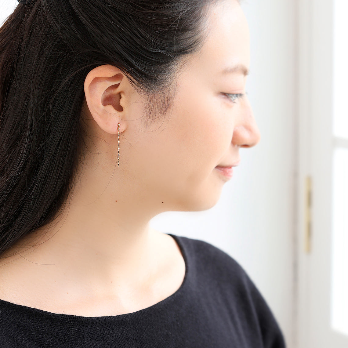 存在感のあるK18ペタルチェーンピアスを着用した耳元。地金のみのシンプルなデザインと軽やかな着け心地が魅力の、山梨県甲府市で製作したMITUREのゴールドジュエリー。